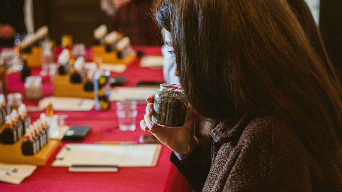 O participantă la atelierul de parfumerie miroase plante uscate dintr-un borcan, la o masă cu flacoane de ingrediente