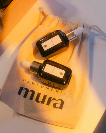 Două sticluțe cu esențele Ambră gri și Piper roz pe săculețul cu logo Parfumeria Mura