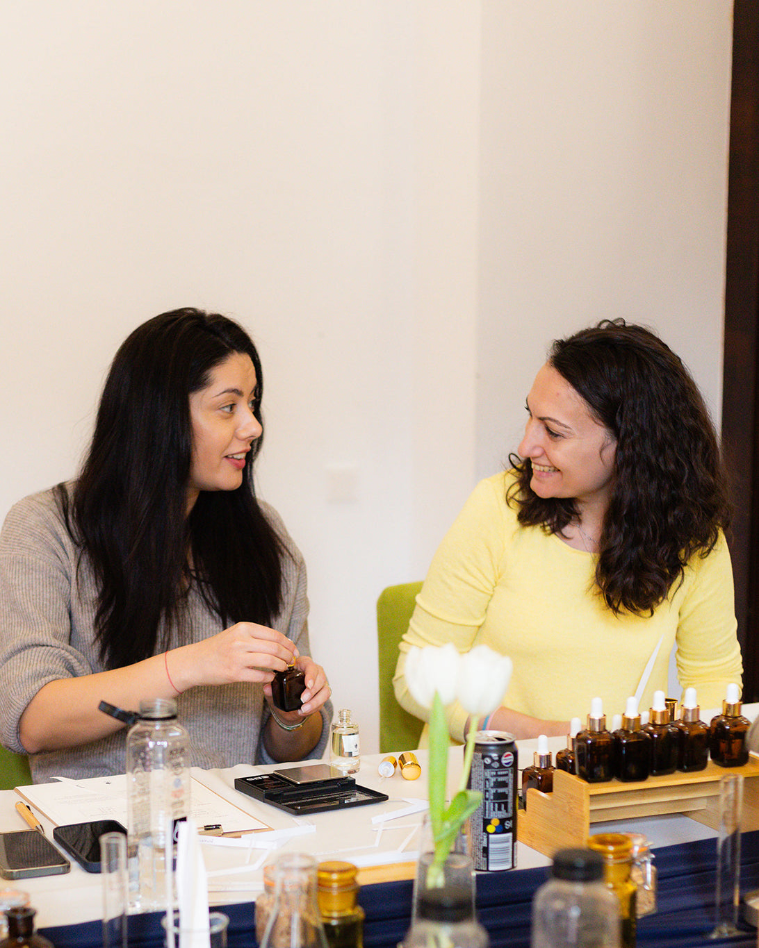 Două participante stau de vorbă la atelierul de parfum în timp ce își creează propriul parfum