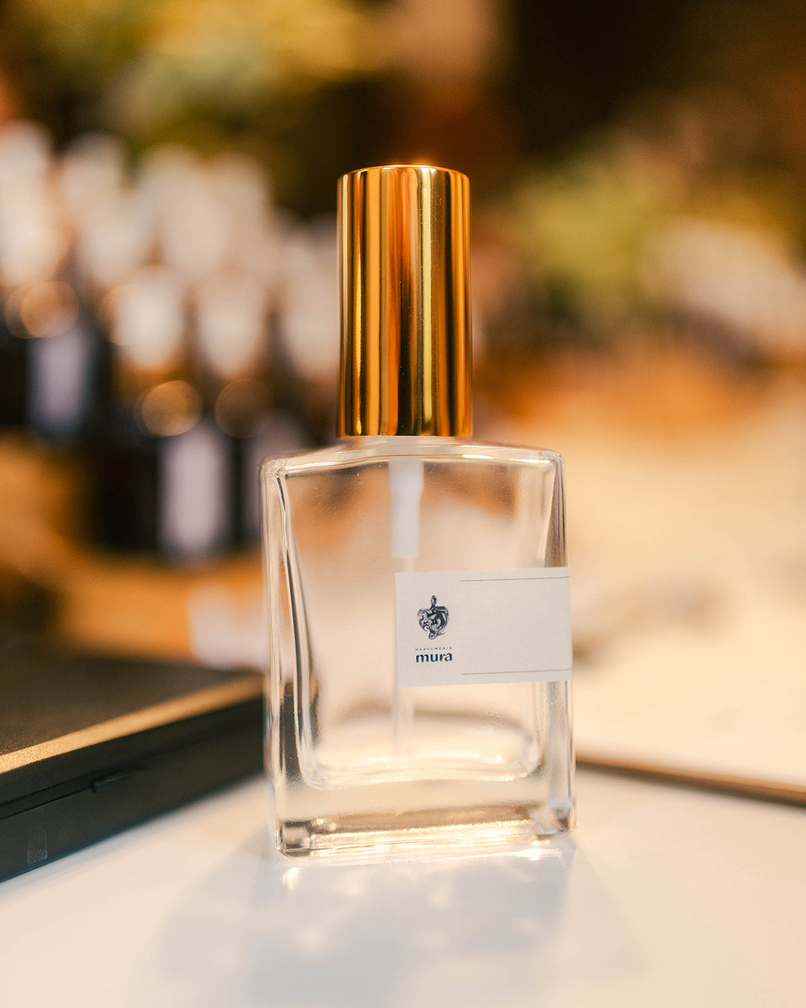 Sticluța de parfum cu eticheta Parfumeria Mura și pulverizator auriu, pe masa de lucru a atelierului