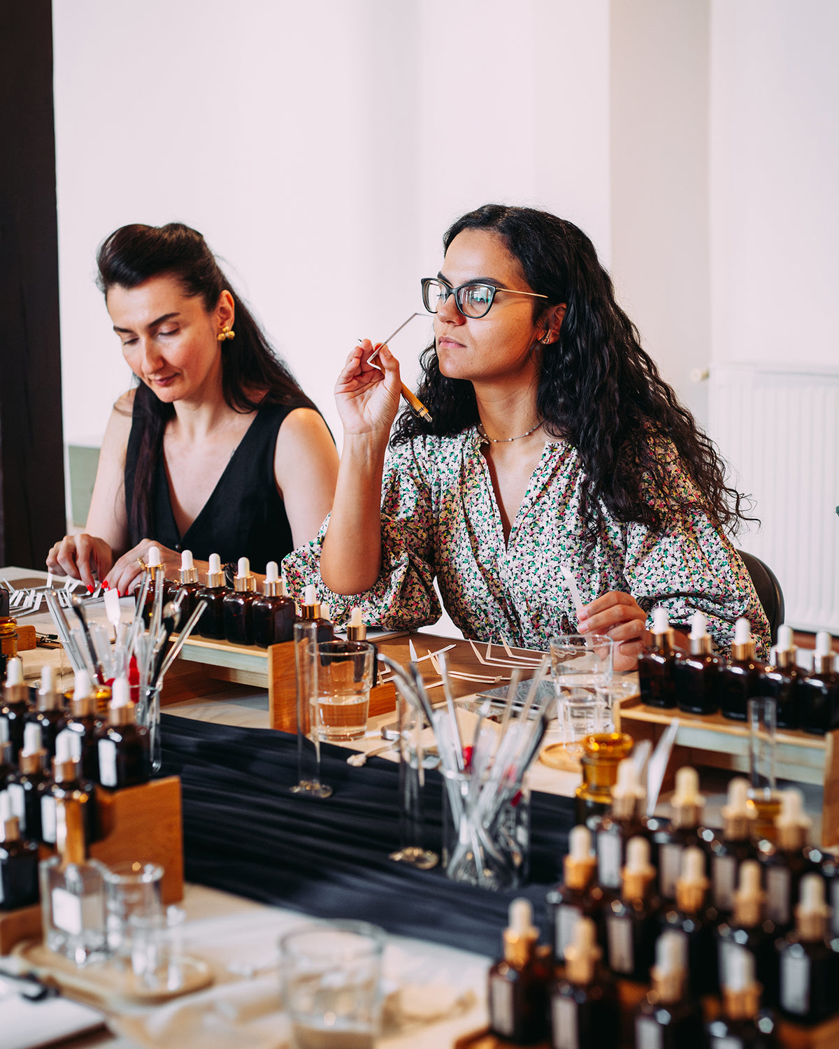 Două participante la atelierul de parfum: una miroase un blotter, cealaltă își aranjează blotterele etichetate