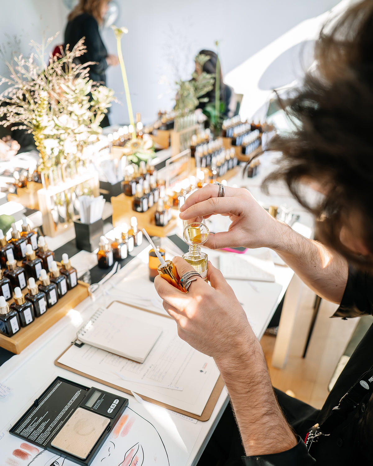 Participant creându-și parfumul la atelier: umple sticluța de parfum cu pulverizator, lângă caiet și cântar