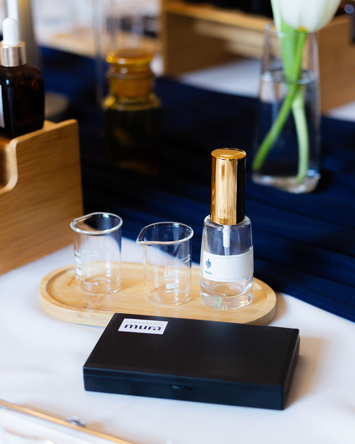 Masă de lucru la atelierul de grup: pahare gradate, sticluță de parfum și cutie cu logo Parfumeria Mura