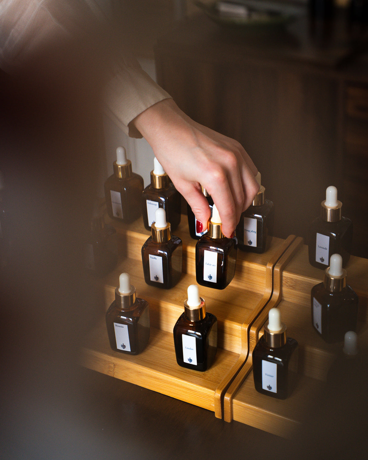 Mână alegând esența de zahăr ars din suportul cu sticluțe etichetate, la atelierul de parfum